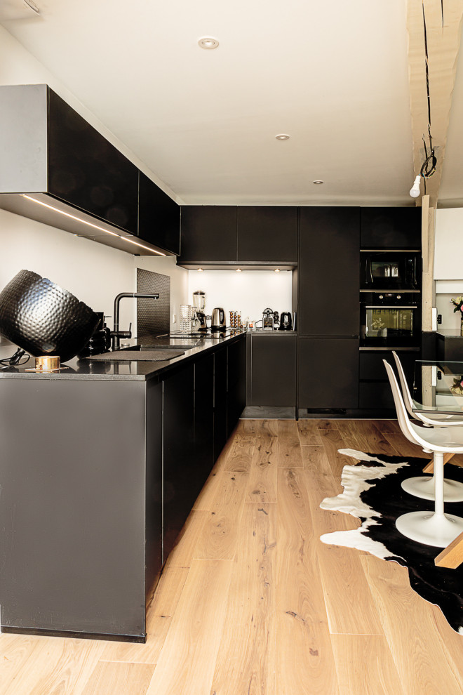 Inspiration for an expansive contemporary l-shaped open plan kitchen in Other with a submerged sink, granite worktops, black splashback, black appliances, no island, brown floors, black worktops and exposed beams.