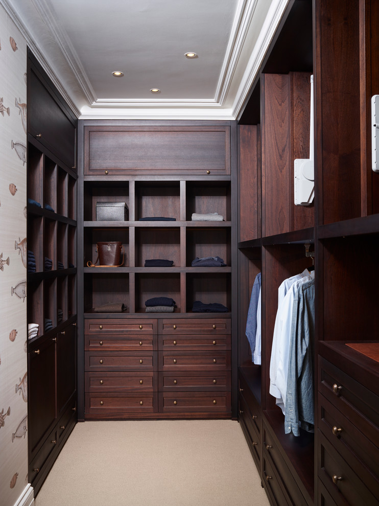 Traditional men's walk-in wardrobe in London with dark wood cabinets, carpet, shaker cabinets and beige floor.