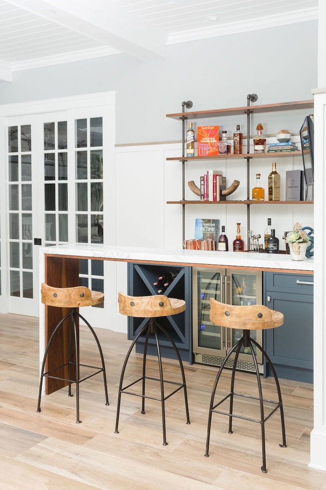 Inspiration for a small transitional single-wall wet bar in San Diego with shaker cabinets, blue cabinets, marble benchtops, white splashback, timber splashback, light hardwood floors, brown floor and white benchtop.