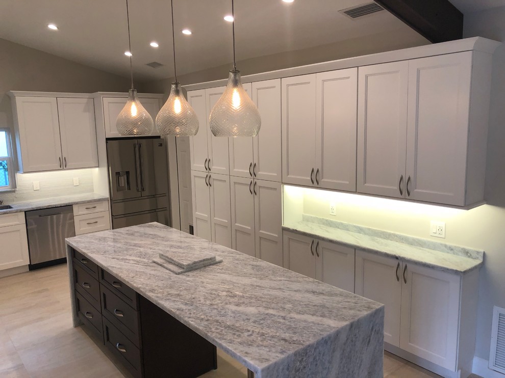 Kitchen - mid-sized transitional u-shaped beige floor kitchen idea in Miami with an undermount sink, recessed-panel cabinets, white cabinets, gray backsplash, glass tile backsplash, stainless steel appliances, an island and gray countertops