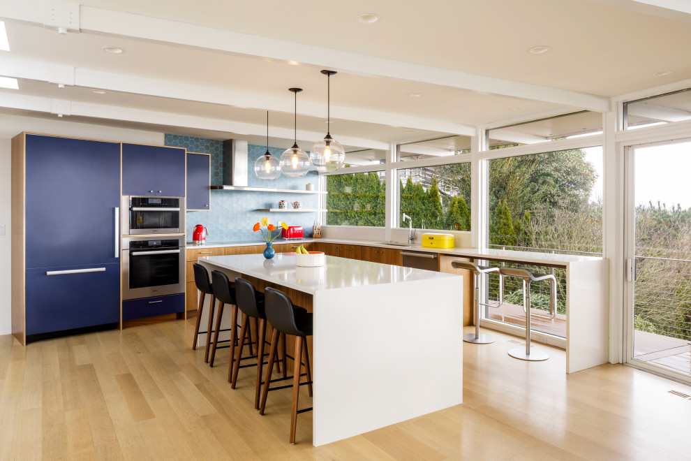 Photo of a contemporary u-shaped eat-in kitchen in Portland with a drop-in sink, medium wood cabinets, quartz benchtops, blue splashback, ceramic splashback, stainless steel appliances, light hardwood floors, with island, white benchtop and exposed beam.