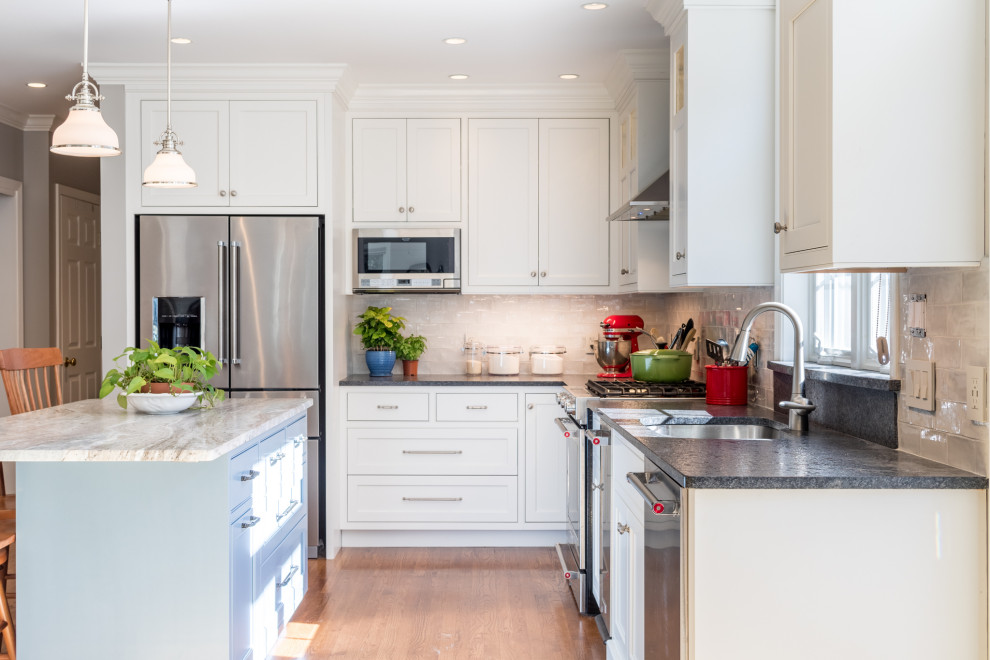 Transitional l-shaped kitchen photo with blue cabinets, granite countertops, white backsplash, stainless steel appliances, an island and multicolored countertops