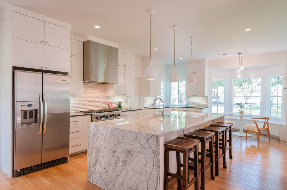 This is an example of a transitional eat-in kitchen in Dallas with a farmhouse sink, flat-panel cabinets, white cabinets, white splashback, porcelain splashback, stainless steel appliances, medium hardwood floors and with island.