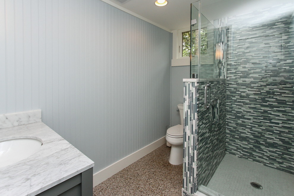 Small beach style 3/4 bathroom in Atlanta with furniture-like cabinets, grey cabinets, a corner shower, a two-piece toilet, multi-coloured tile, glass sheet wall, blue walls, an undermount sink and marble benchtops.