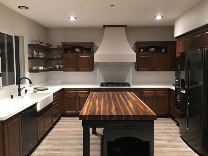 Mid-sized contemporary u-shaped separate kitchen in Los Angeles with a farmhouse sink, recessed-panel cabinets, dark wood cabinets, wood benchtops, white splashback, stone tile splashback, black appliances, light hardwood floors, with island, grey floor and brown benchtop.