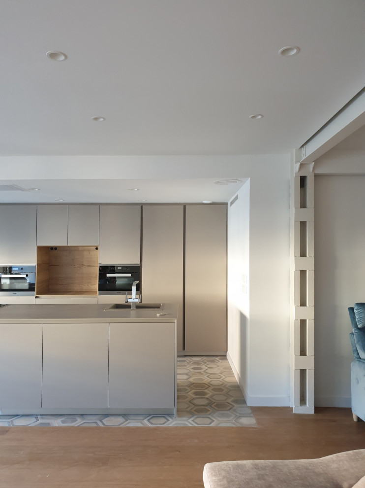 Photo of an expansive contemporary single-wall open plan kitchen in Valencia with a single-bowl sink, flat-panel cabinets, beige cabinets, limestone benchtops, black appliances, limestone floors, with island, grey floor and grey benchtop.
