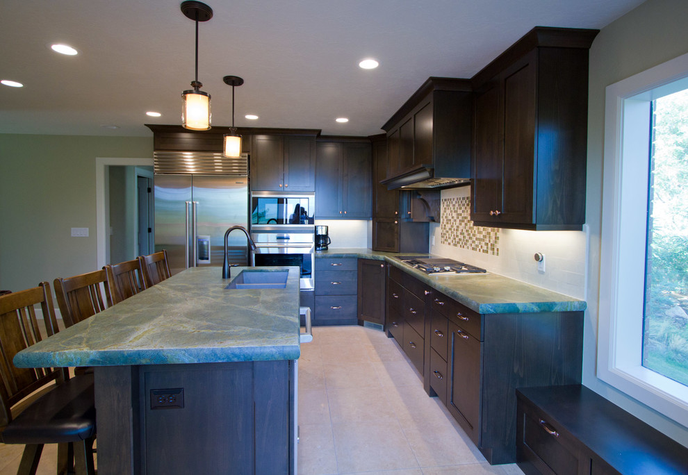 Mid-sized transitional l-shaped eat-in kitchen in Salt Lake City with a double-bowl sink, shaker cabinets, dark wood cabinets, quartzite benchtops, white splashback, stone tile splashback, stainless steel appliances, limestone floors and with island.