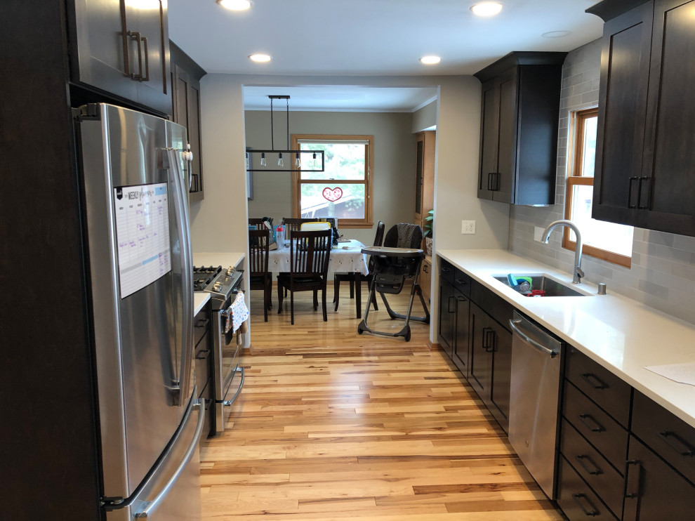 Example of a mid-sized transitional galley light wood floor and brown floor eat-in kitchen design with an undermount sink, shaker cabinets, black cabinets, quartz countertops, gray backsplash, subway tile backsplash, stainless steel appliances, no island and white countertops