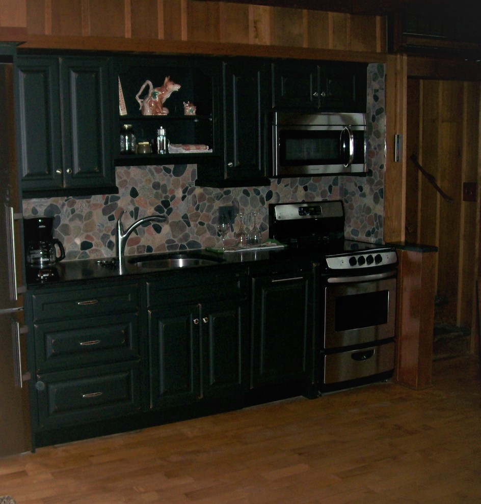 Example of a mid-sized mountain style single-wall medium tone wood floor enclosed kitchen design with an undermount sink, raised-panel cabinets, black cabinets, granite countertops, gray backsplash, stone tile backsplash, stainless steel appliances and no island