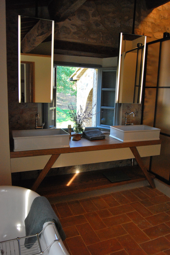 Стильный дизайн: большая главная ванная комната в классическом стиле с открытыми фасадами, бежевыми фасадами, ванной на ножках, душем без бортиков, раздельным унитазом, бежевой плиткой, плиткой из известняка, бежевыми стенами, кирпичным полом, настольной раковиной, столешницей из дерева, коричневым полом, душем с распашными дверями, коричневой столешницей, тумбой под две раковины, встроенной тумбой, балками на потолке и кирпичными стенами - последний тренд