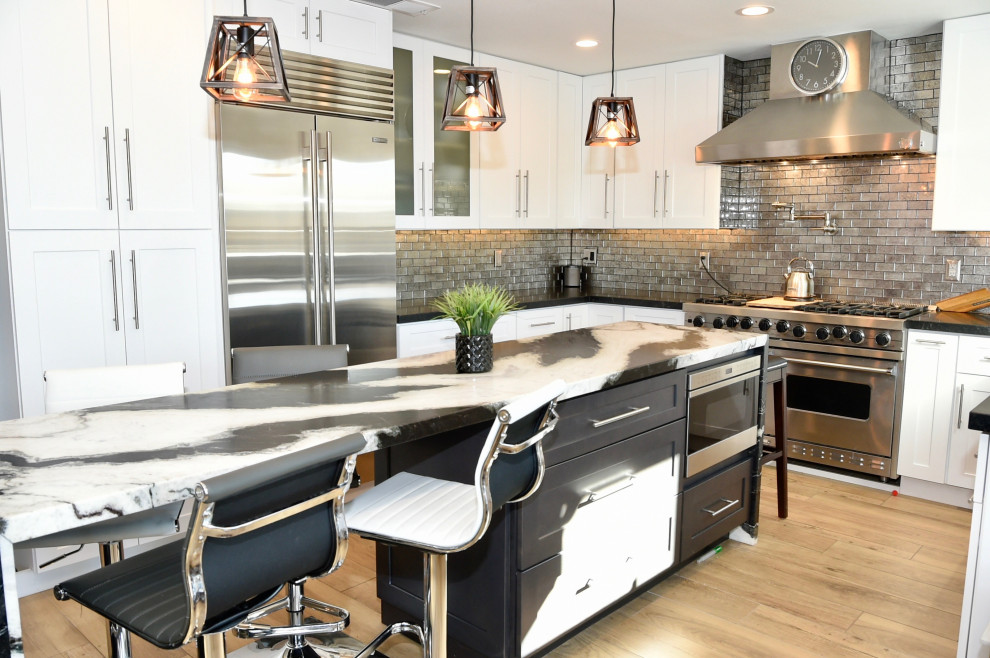 Photo of a mid-sized modern u-shaped eat-in kitchen in Phoenix with an undermount sink, shaker cabinets, white cabinets, granite benchtops, metallic splashback, glass sheet splashback, stainless steel appliances, porcelain floors, with island, beige floor and multi-coloured benchtop.