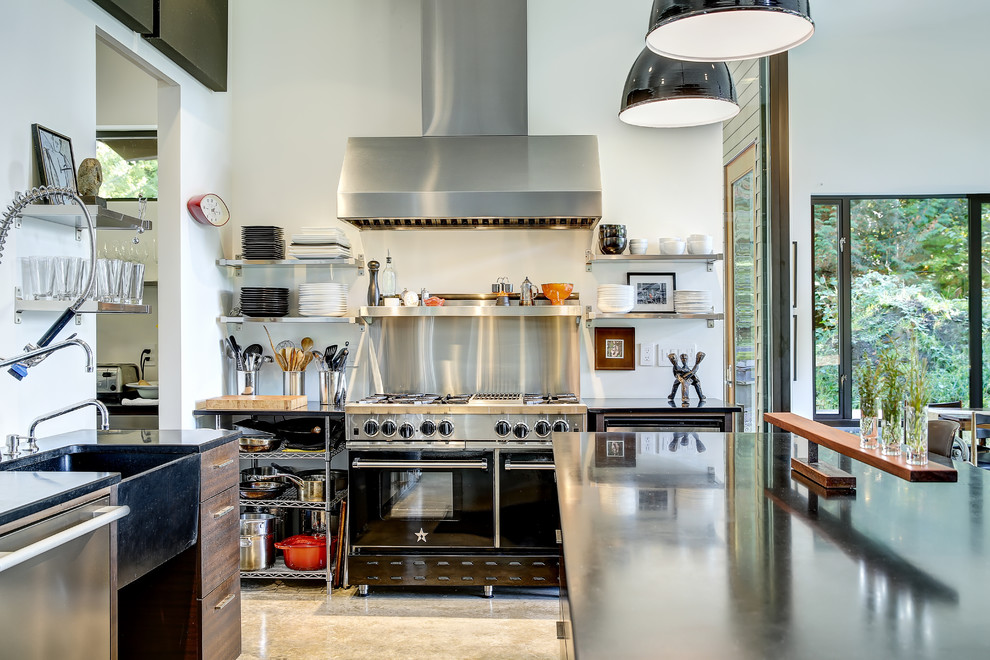Inspiration for an industrial l-shaped open plan kitchen in Seattle with a farmhouse sink, open cabinets, stainless steel cabinets, black appliances, concrete floors, with island and grey floor.