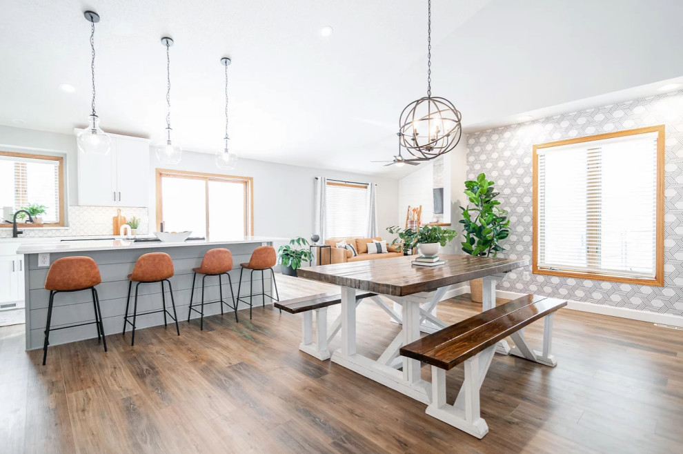 This is an example of a large scandinavian l-shaped eat-in kitchen in Minneapolis with a double-bowl sink, shaker cabinets, white cabinets, quartz benchtops, white splashback, ceramic splashback, stainless steel appliances, medium hardwood floors, with island, brown floor and white benchtop.