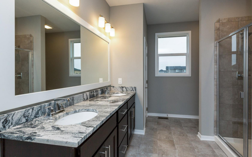 Inspiration for a large transitional master ceramic tile and brown floor drop-in bathtub remodel with shaker cabinets, dark wood cabinets, a two-piece toilet, gray walls, an undermount sink, granite countertops, a hinged shower door and multicolored countertops