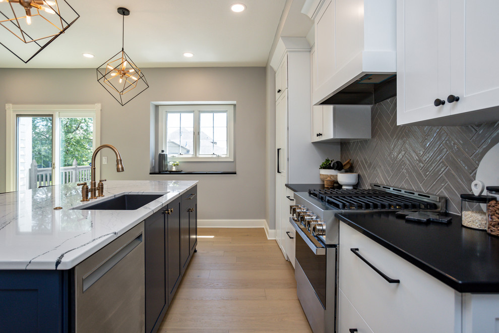 Large transitional l-shaped light wood floor and brown floor eat-in kitchen photo in Other with an undermount sink, recessed-panel cabinets, white cabinets, quartz countertops, gray backsplash, ceramic backsplash, stainless steel appliances, an island and black countertops