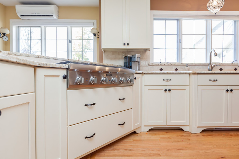 Mid-sized transitional u-shaped light wood floor enclosed kitchen photo in Boston with a double-bowl sink, recessed-panel cabinets, white cabinets, granite countertops, beige backsplash, stone tile backsplash, stainless steel appliances and an island