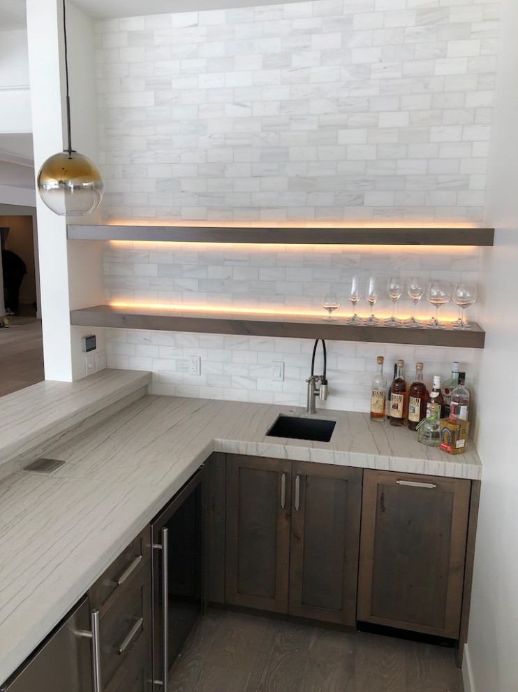 Photo of a large contemporary l-shaped seated home bar in Salt Lake City with an undermount sink, shaker cabinets, brown cabinets, quartzite benchtops, white splashback, subway tile splashback, light hardwood floors and white benchtop.