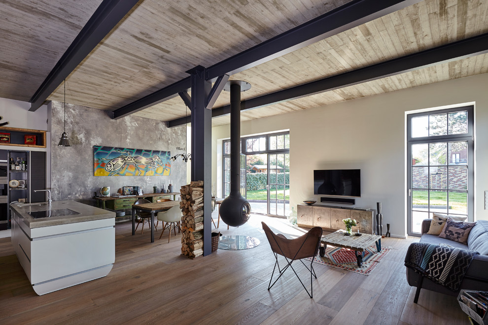 Industrial loft-style living room in Cologne with white walls, dark hardwood floors, a hanging fireplace, a metal fireplace surround, a wall-mounted tv and brown floor.