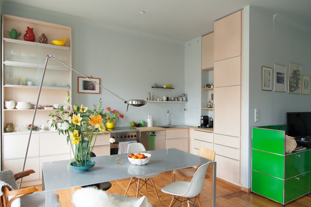 Mid-sized scandinavian l-shaped eat-in kitchen in Berlin with flat-panel cabinets, beige cabinets, wood benchtops, blue splashback, no island, a drop-in sink, stainless steel appliances, light hardwood floors and brown floor.