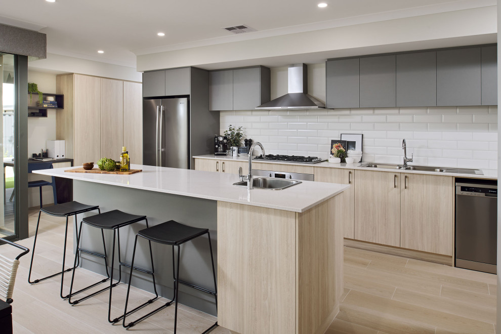 This is an example of a contemporary galley kitchen in Perth with a drop-in sink, flat-panel cabinets, light wood cabinets, white splashback, subway tile splashback, stainless steel appliances, light hardwood floors, with island, beige floor and white benchtop.