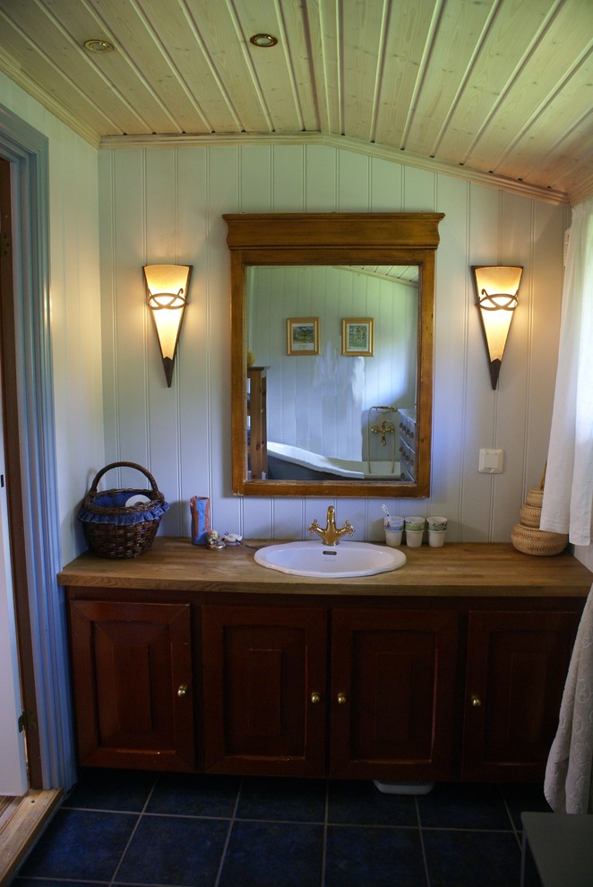 Mid-sized traditional master bathroom in Other with a drop-in sink, raised-panel cabinets, medium wood cabinets, wood benchtops, a claw-foot tub, a one-piece toilet, blue tile, ceramic tile, blue walls and ceramic floors.