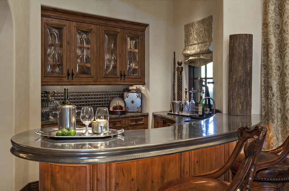 Photo of a large mediterranean u-shaped seated home bar in Phoenix with an undermount sink, raised-panel cabinets, distressed cabinets, zinc benchtops, grey splashback and stone tile splashback.