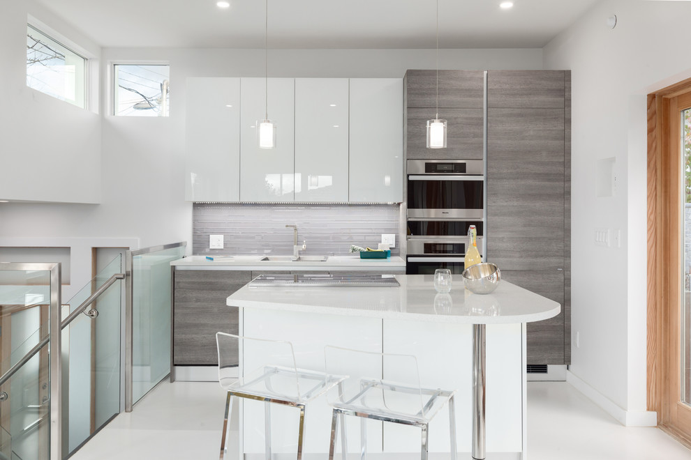 Photo of a small contemporary u-shaped eat-in kitchen in Vancouver with flat-panel cabinets, light wood cabinets, grey splashback, stainless steel appliances, with island, an undermount sink, quartz benchtops, matchstick tile splashback, concrete floors, white floor and white benchtop.