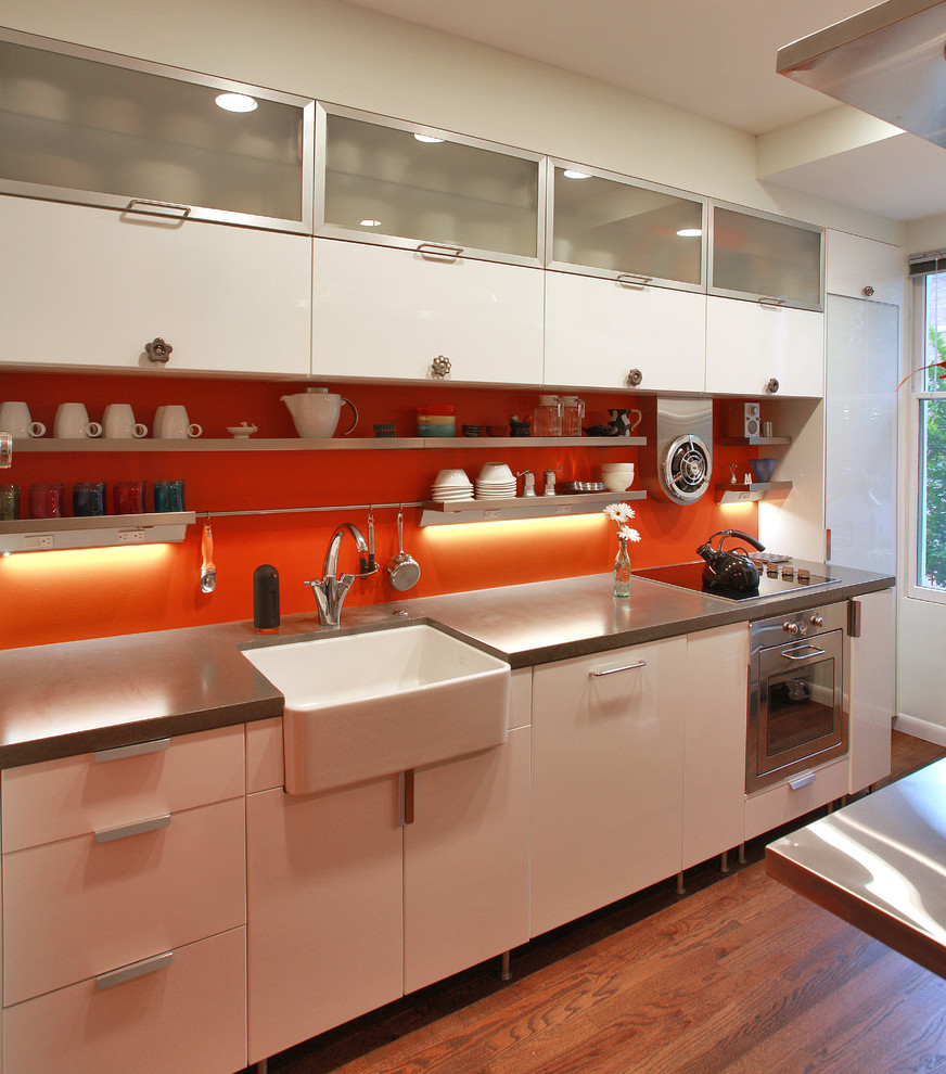 Design ideas for an industrial kitchen in DC Metro with a farmhouse sink, stainless steel appliances, flat-panel cabinets, white cabinets and orange splashback.