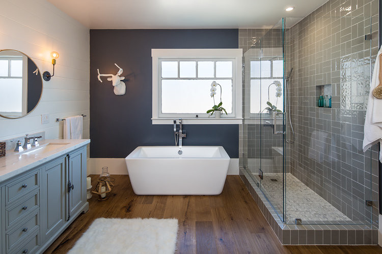 Design ideas for a large industrial master bathroom in San Francisco with recessed-panel cabinets, grey cabinets, a freestanding tub, a corner shower, a two-piece toilet, gray tile, ceramic tile, white walls, medium hardwood floors, a drop-in sink and laminate benchtops.