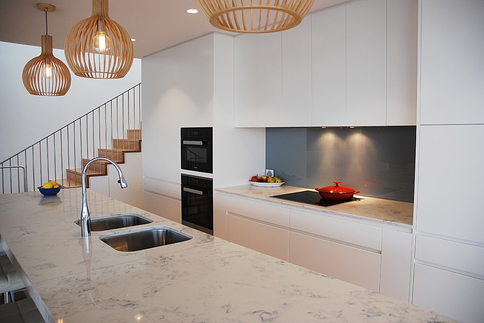 Photo of a large contemporary single-wall eat-in kitchen in Sydney with an undermount sink, flat-panel cabinets, white cabinets, quartz benchtops, blue splashback, glass sheet splashback, black appliances, medium hardwood floors and with island.
