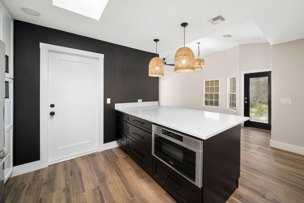 Photo of a medium sized modern l-shaped kitchen/diner in Atlanta with a belfast sink, shaker cabinets, black cabinets, granite worktops, white splashback, granite splashback, stainless steel appliances, painted wood flooring, an island and brown floors.