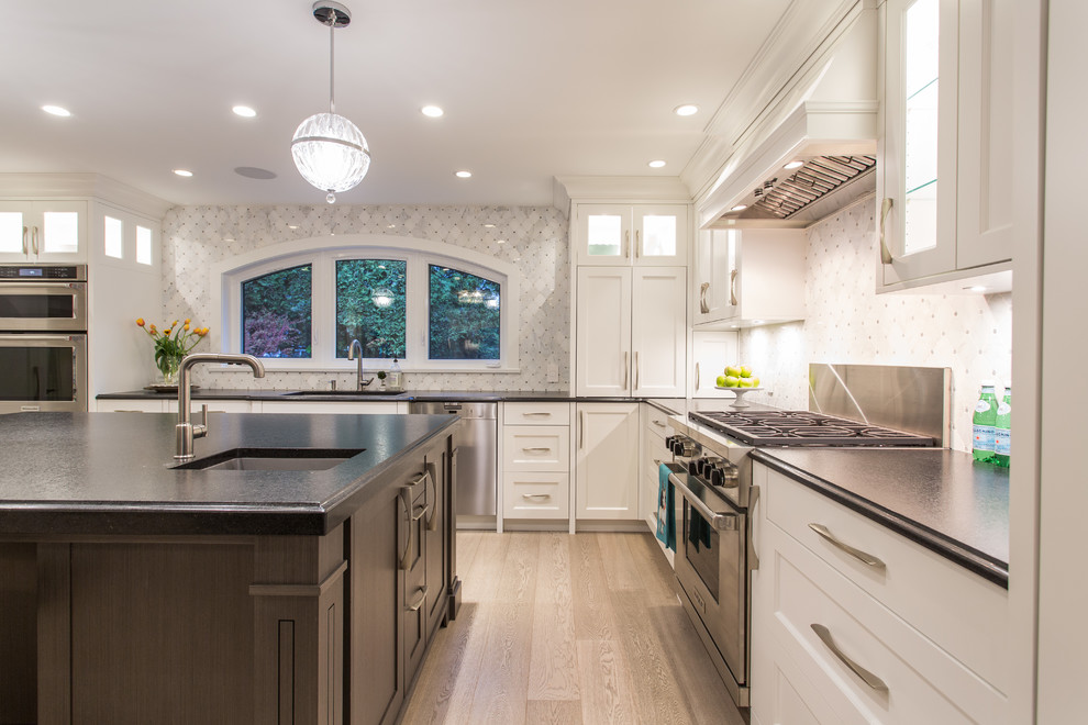 Eat-in kitchen - large transitional l-shaped medium tone wood floor and beige floor eat-in kitchen idea in Vancouver with an undermount sink, shaker cabinets, white cabinets, granite countertops, gray backsplash, marble backsplash, stainless steel appliances, an island and black countertops