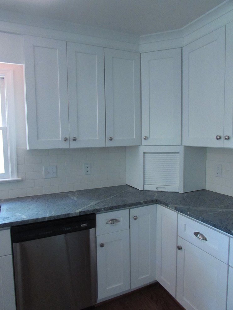 Mid-sized transitional l-shaped medium tone wood floor enclosed kitchen photo with an undermount sink, shaker cabinets, white cabinets, soapstone countertops, white backsplash, subway tile backsplash, stainless steel appliances and a peninsula