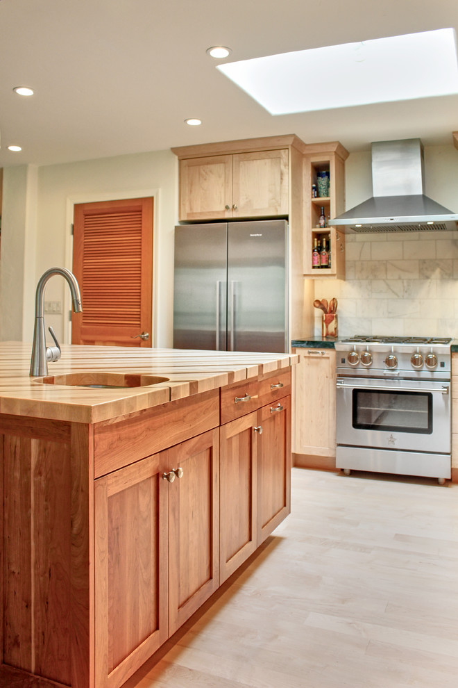 Eat-in kitchen - mid-sized transitional l-shaped light wood floor and brown floor eat-in kitchen idea with a farmhouse sink, shaker cabinets, medium tone wood cabinets, wood countertops, white backsplash, marble backsplash, stainless steel appliances and an island