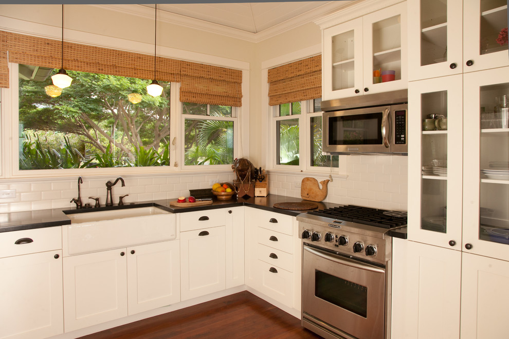 Inspiration for a mid-sized tropical u-shaped kitchen pantry in Hawaii with a farmhouse sink, flat-panel cabinets, white cabinets, solid surface benchtops, white splashback, ceramic splashback, stainless steel appliances, dark hardwood floors and no island.