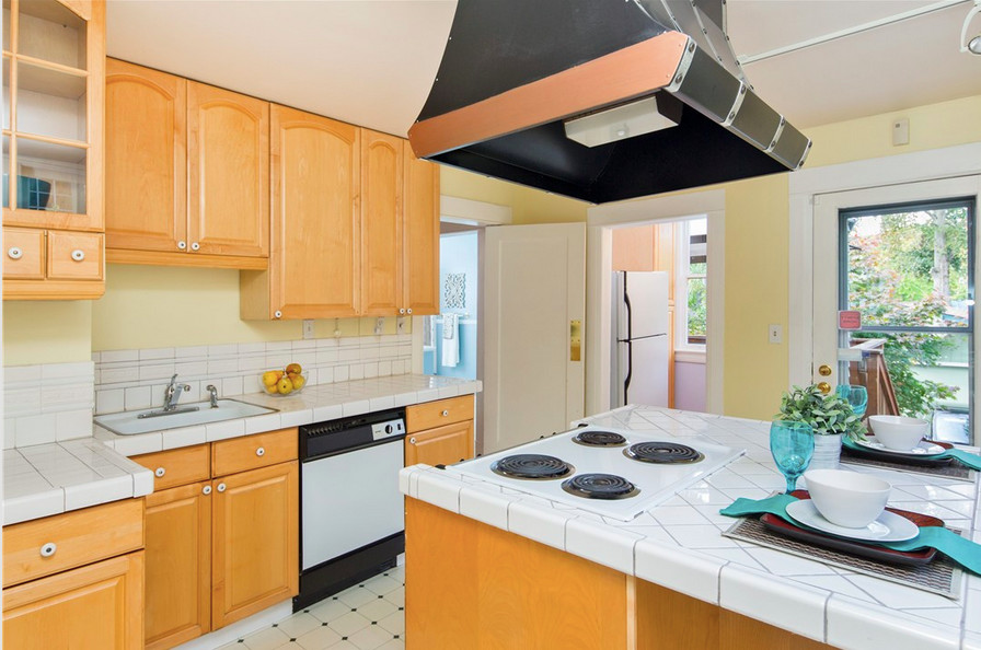 Mid-sized traditional galley separate kitchen in Seattle with an undermount sink, shaker cabinets, medium wood cabinets, tile benchtops, white splashback, ceramic splashback, black appliances, ceramic floors and with island.