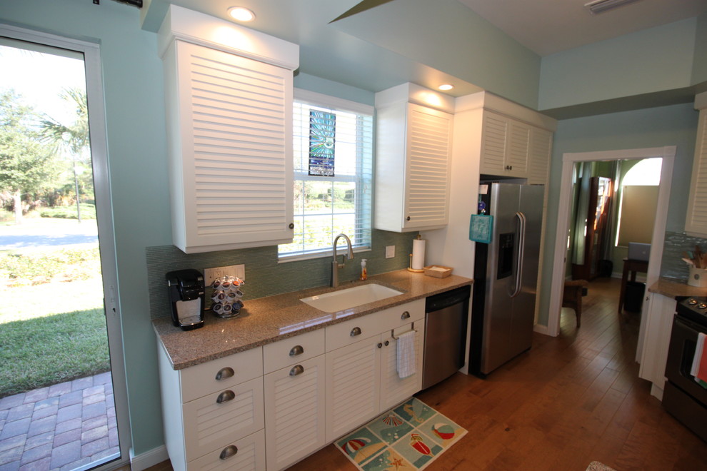 Photo of a mid-sized transitional galley eat-in kitchen in Tampa with a drop-in sink, louvered cabinets, white cabinets, blue splashback, glass tile splashback, stainless steel appliances and medium hardwood floors.