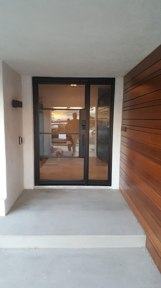 Aménagement d'une porte d'entrée moderne en bois de taille moyenne avec un mur marron, sol en béton ciré, une porte simple, une porte noire et un sol gris.