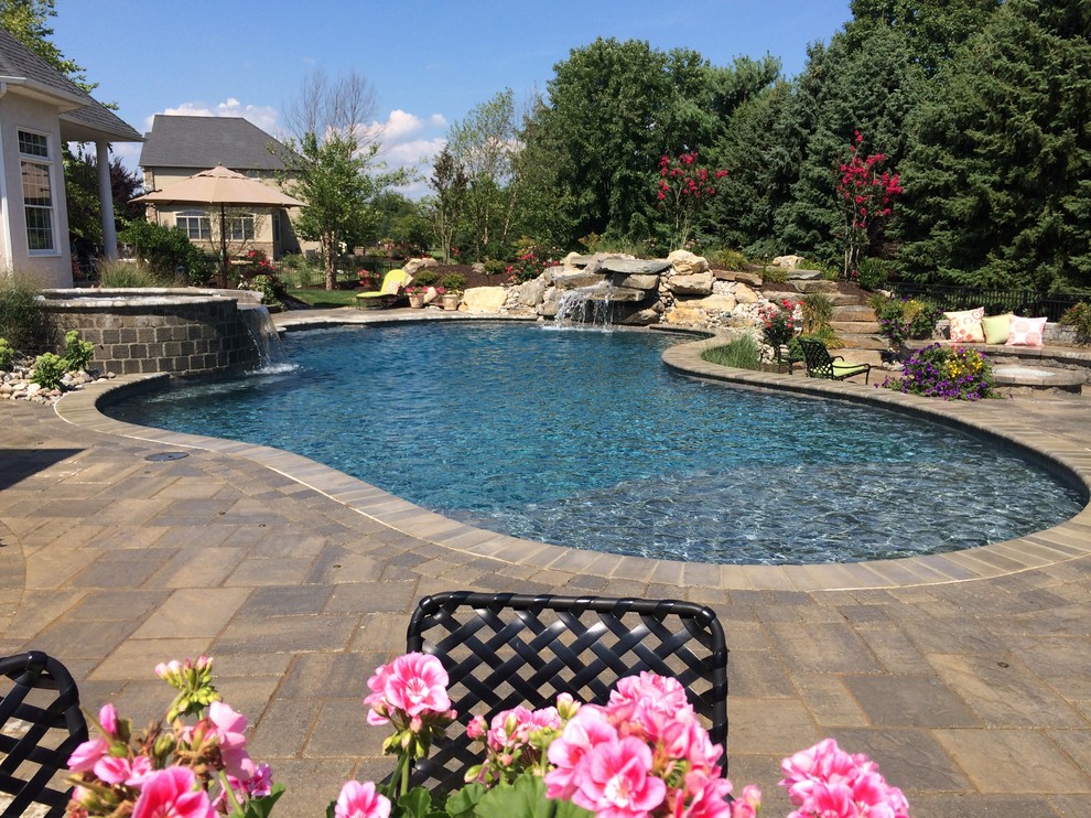 Inspiration for a large traditional backyard custom-shaped natural pool in Philadelphia with concrete pavers.