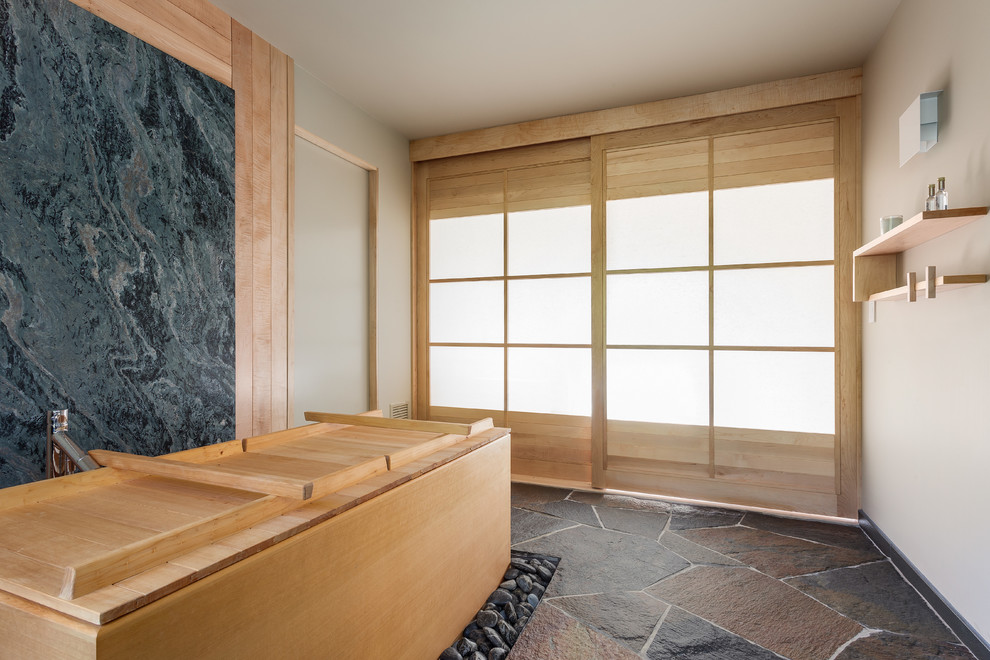 Photo of a mid-sized asian master bathroom in New York with furniture-like cabinets, light wood cabinets, a japanese tub, multi-coloured tile, stone tile, beige walls and slate floors.