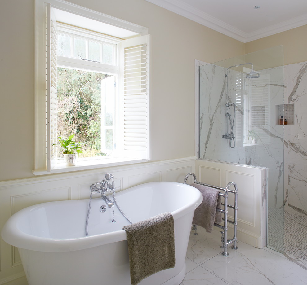 This is an example of a large traditional master wet room bathroom in Dublin with recessed-panel cabinets, grey cabinets, a freestanding tub, a wall-mount toilet, white tile, porcelain tile, white walls, porcelain floors, an undermount sink and marble benchtops.