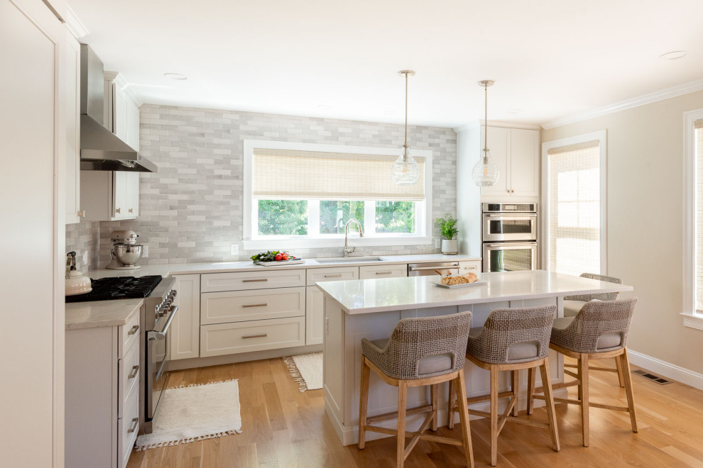 Inspiration for a huge transitional l-shaped light wood floor and brown floor open concept kitchen remodel in Boston with an undermount sink, shaker cabinets, white cabinets, quartz countertops, gray backsplash, subway tile backsplash, stainless steel appliances, an island and white countertops