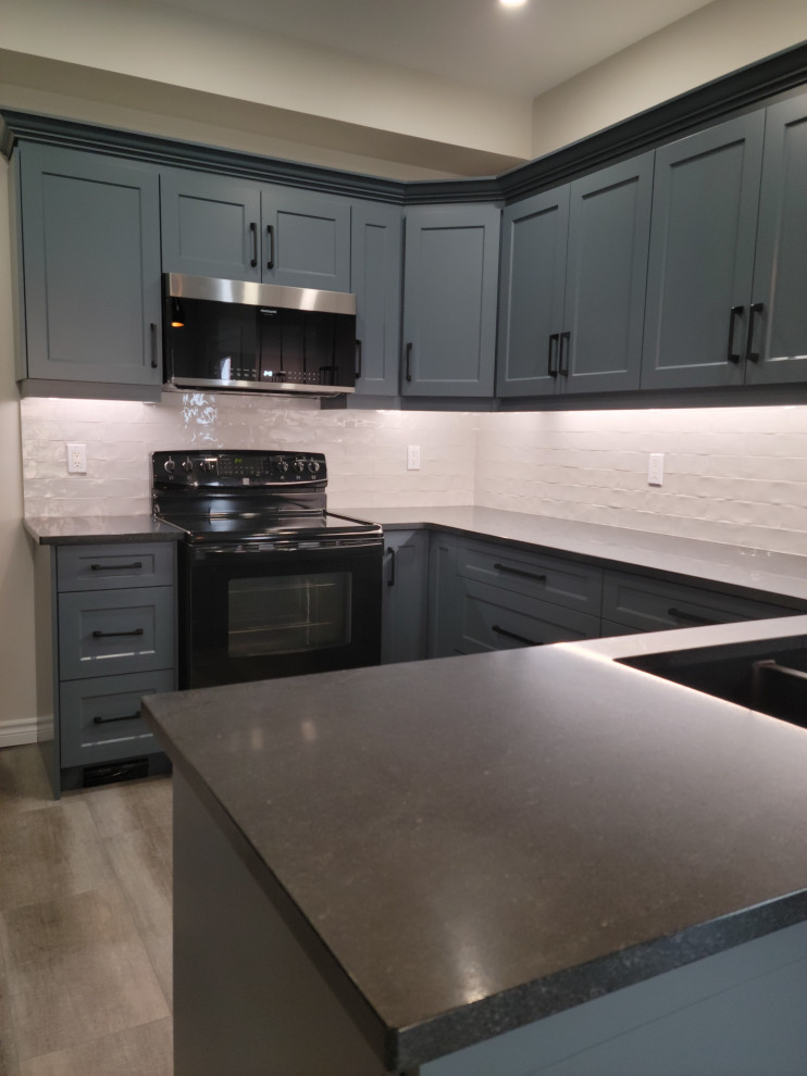 Eat-in kitchen - mid-sized transitional u-shaped vinyl floor eat-in kitchen idea with an undermount sink, recessed-panel cabinets, blue cabinets, quartzite countertops, white backsplash, porcelain backsplash, black appliances, a peninsula and black countertops