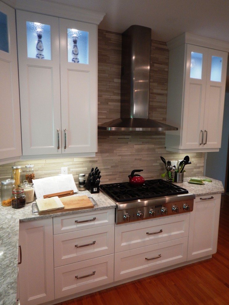 Example of a large transitional l-shaped light wood floor eat-in kitchen design with an undermount sink, recessed-panel cabinets, white cabinets, quartz countertops, gray backsplash, stone tile backsplash, stainless steel appliances and an island