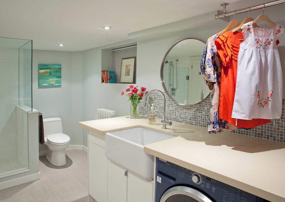 Photo of a large contemporary single-wall utility room in Toronto with a farmhouse sink, flat-panel cabinets, white cabinets, blue walls, a side-by-side washer and dryer and beige floor.