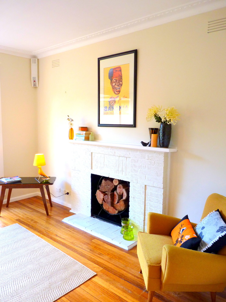 Photo of a mid-sized midcentury enclosed living room in Melbourne with yellow walls, light hardwood floors, a standard fireplace, a brick fireplace surround and brown floor.