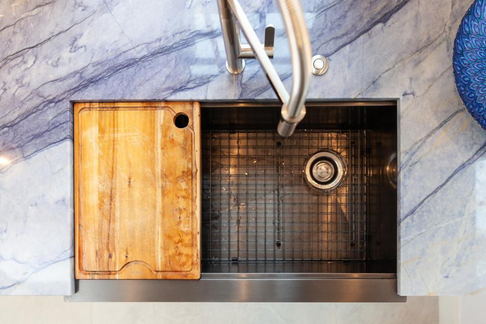 Small modern galley kitchen in Boston with a belfast sink, shaker cabinets, white cabinets, quartz worktops, blue splashback, stainless steel appliances, marble flooring, no island, grey floors and blue worktops.