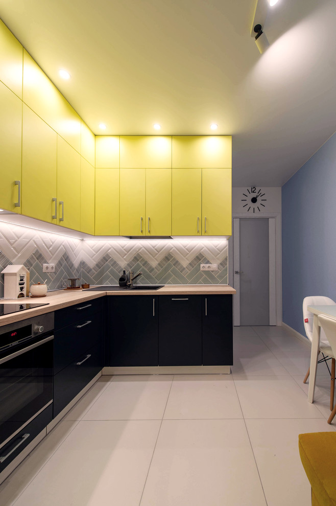 Small contemporary l-shaped separate kitchen in Saint Petersburg with a single-bowl sink, stainless steel appliances, porcelain floors, flat-panel cabinets, yellow cabinets, wood benchtops, grey splashback, no island, white floor and beige benchtop.