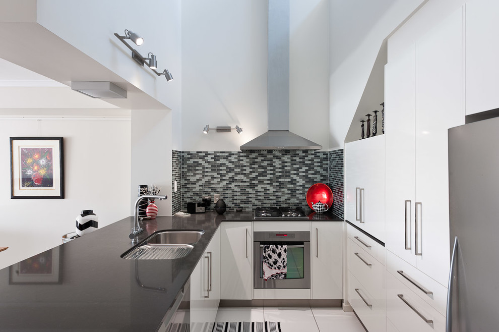 Photo of a mid-sized contemporary l-shaped eat-in kitchen in Brisbane with an undermount sink, flat-panel cabinets, white cabinets, quartzite benchtops, grey splashback, matchstick tile splashback, a peninsula and white floor.