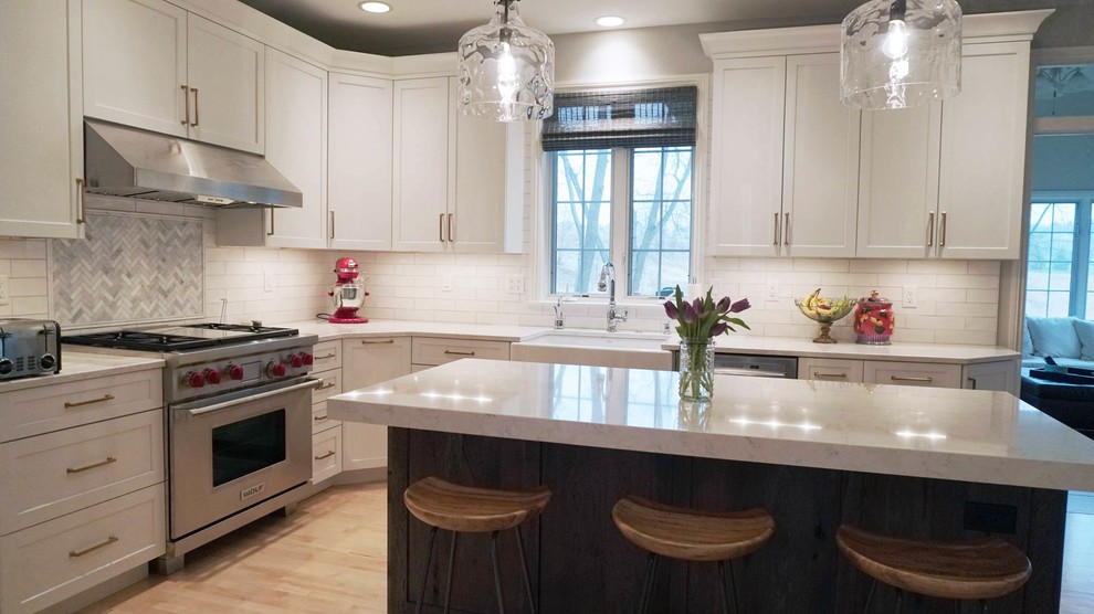 Open concept kitchen - transitional light wood floor open concept kitchen idea with a farmhouse sink, recessed-panel cabinets, white cabinets, white backsplash, subway tile backsplash, stainless steel appliances, an island and white countertops